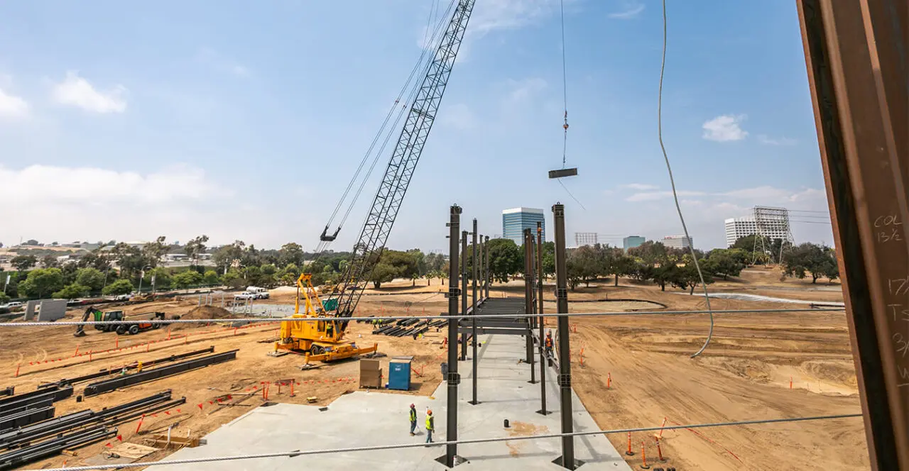 Construction site with a large crane lifting steel beams for the building foundation.