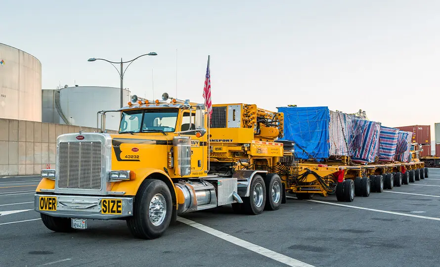 Yellow heavy haul truck transporting oversized load with "oversize" signage.