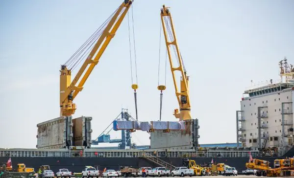 Large cranes lifting sections of a ship hull or large structure at a port.