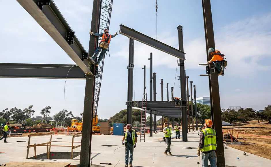 Steelworkers constructing a building frame with a crane lifting beams.