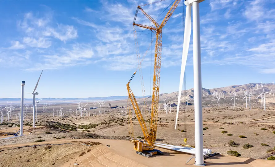 Large crane assembling a wind turbine at a wind farm with many turbines in the background.
