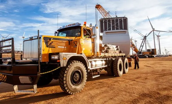 Heavy haul transport truck delivering wind turbine component at renewable energy farm.